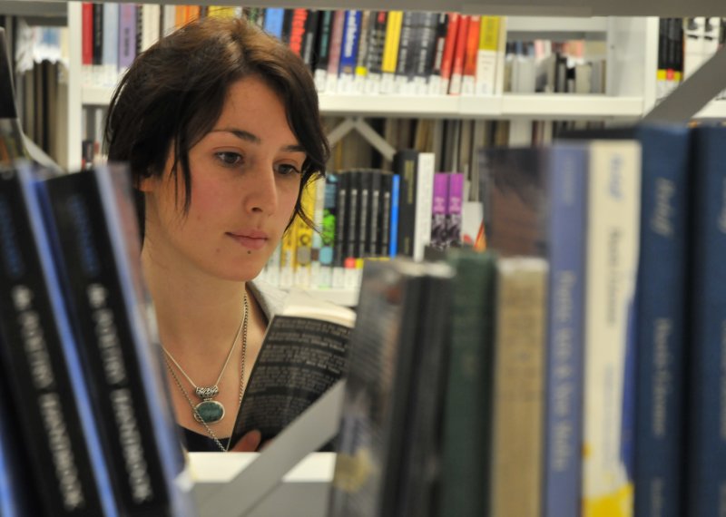 Student's face appearing through a gap in the books in the library.