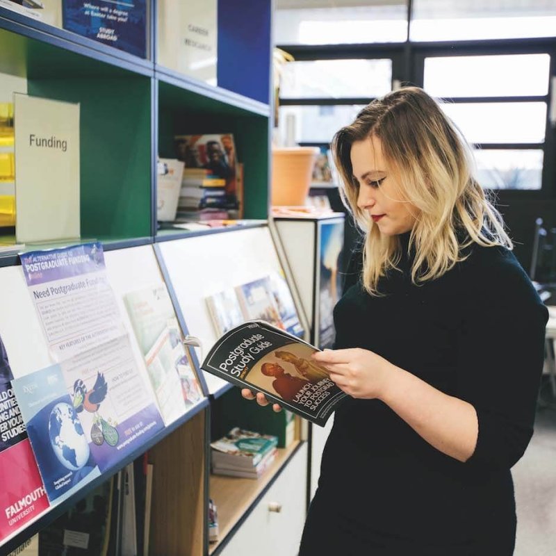 A Falmouth University student looking through a Postgraduate study guide