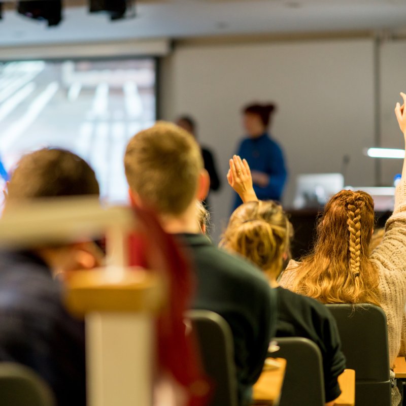 A lecture theatre with students raising their hands