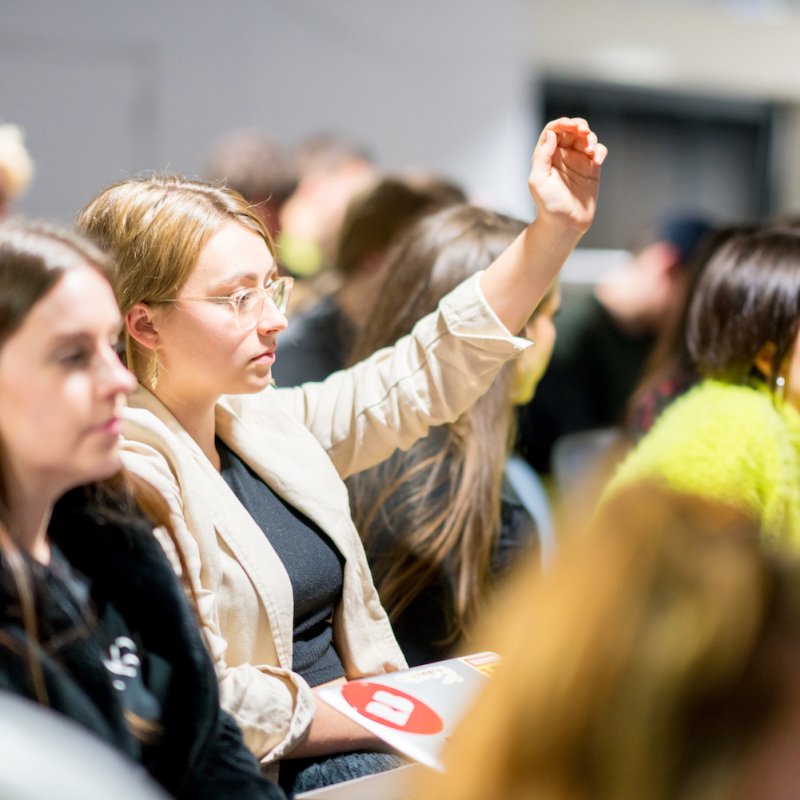 Female student raising hand in a crowd