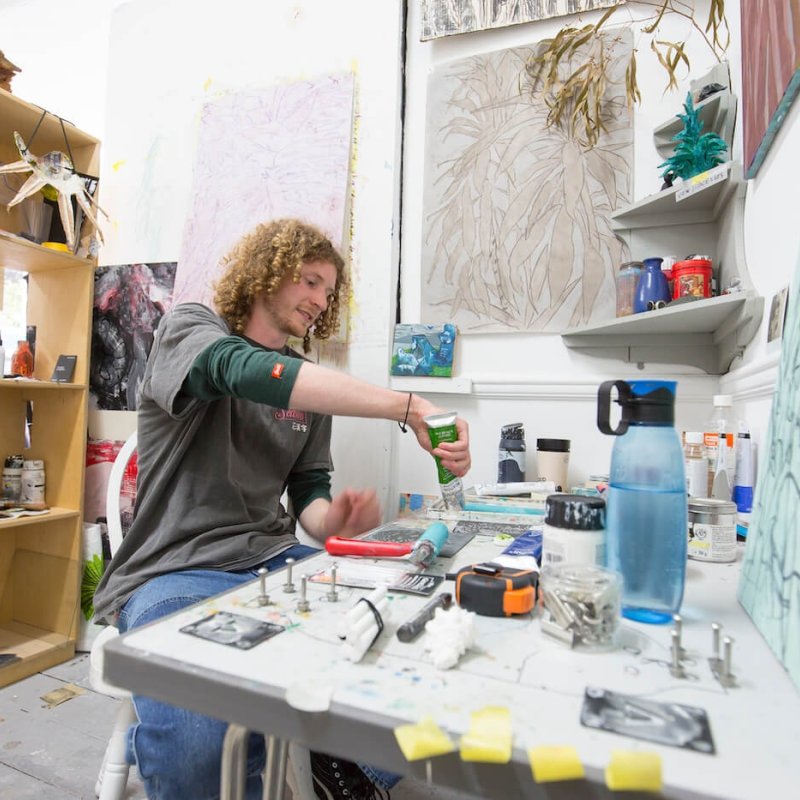 A male student with curly hair sat in a Fine Art studio at Falmouth University