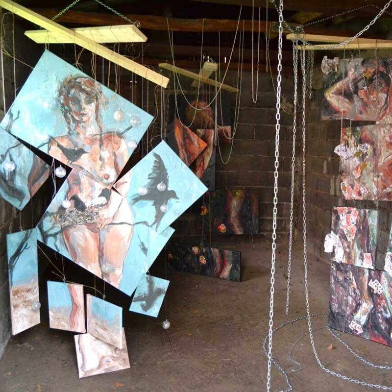 An installation of paintings hanging in a small dark space 