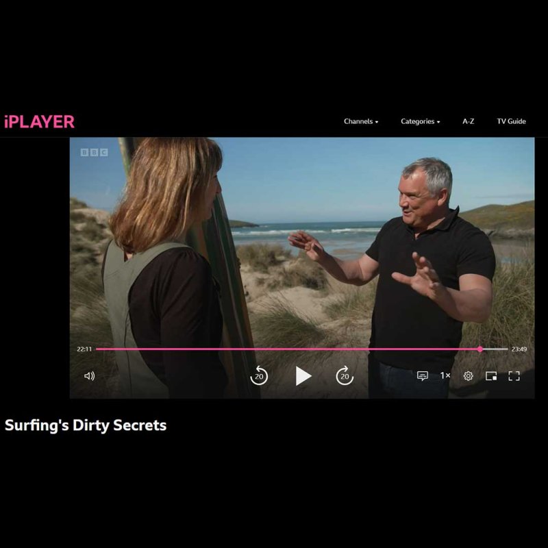 Dr Greg Borne standing on a beach speaking to a surfer 