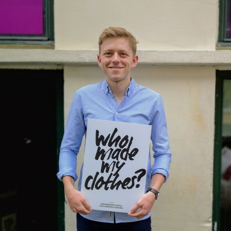 A man stood holding a sign that reads 'Who made my clothes?'