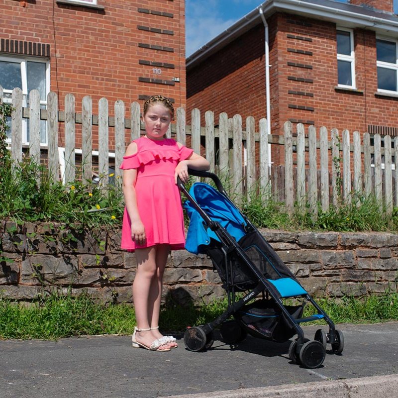 A girl wearing a pink dress standing next to a blue pushchair