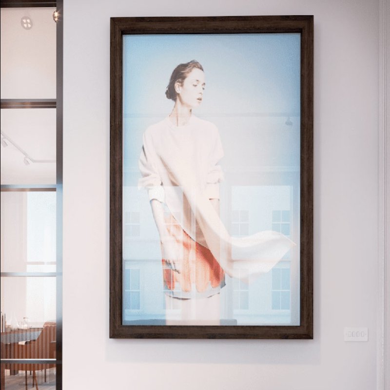 Large picture hung on a wall above a small bench. Picture is of a woman wearing white outfit blowing in the wind against blue background