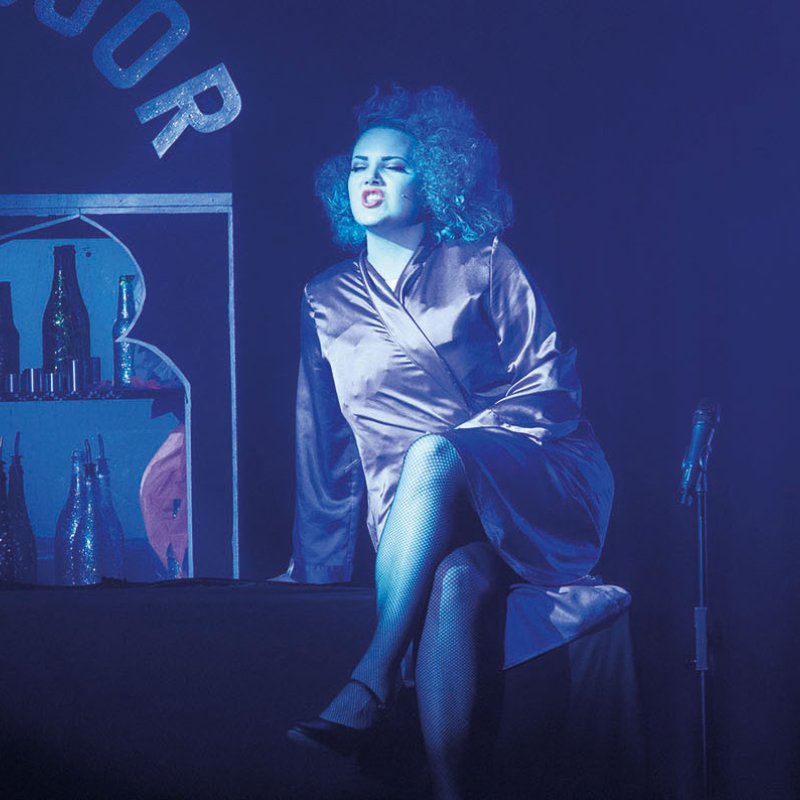 Student on stage in blue lighting and silk gown