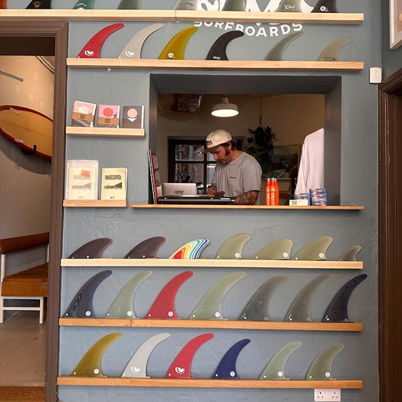 A man in a hatch in the wall with surfboard fins on shelves