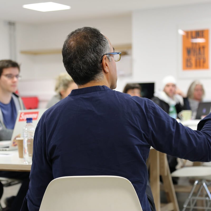 A man in a blue shirt, gesturing to a table of students