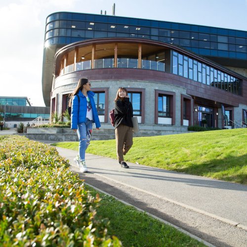 Two female students walking along a path with a large building in the background