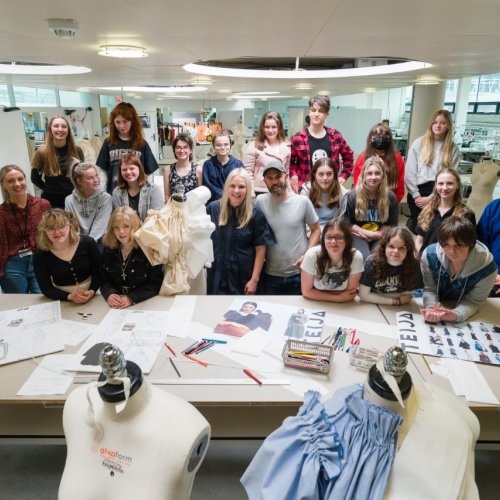 A group of teenagers showcase their artwork - sketches and mannequins with clothing are visible 