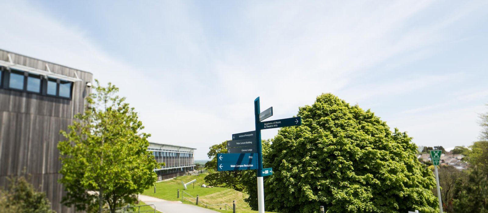 Blue signpost on Penryn Campus with trees and path